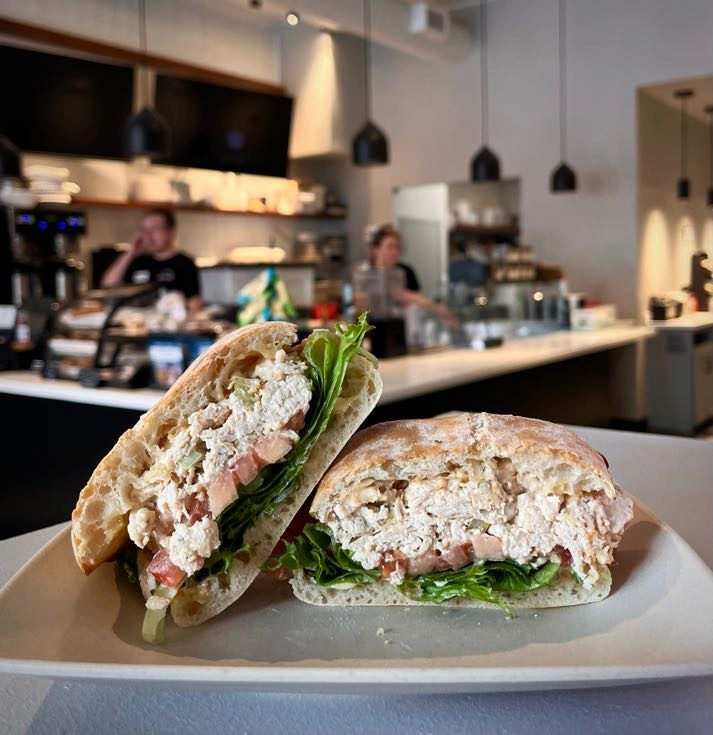 A chicken salad sandwich in the foreground, INspire Cafe team in the background